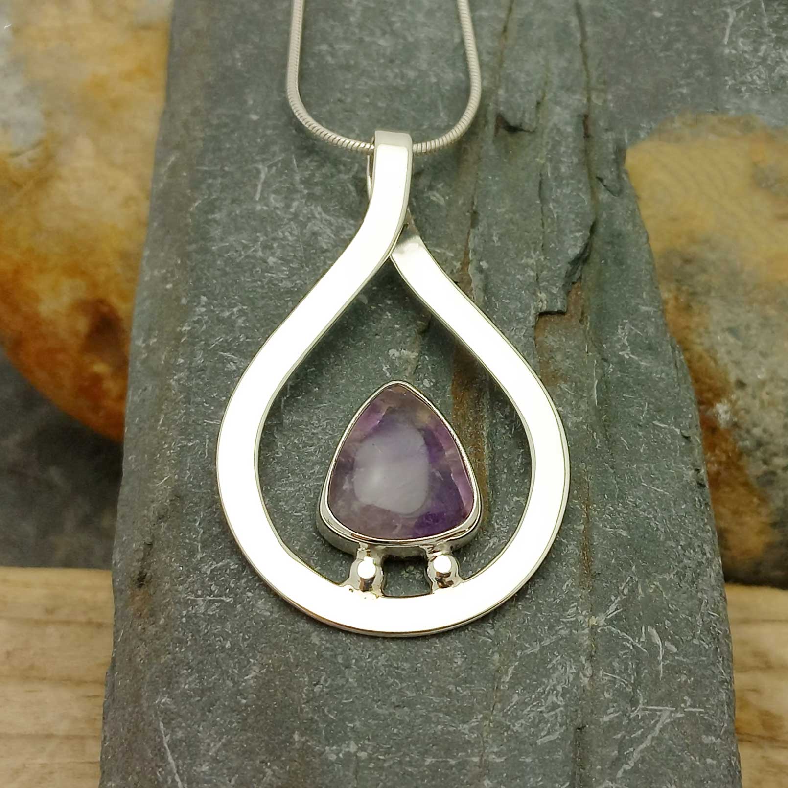 Silver pendant with a purple Amethyst gemstone on a stone background