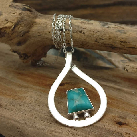 Artisan silver pendant with a turquoise stone on a wooden surface
