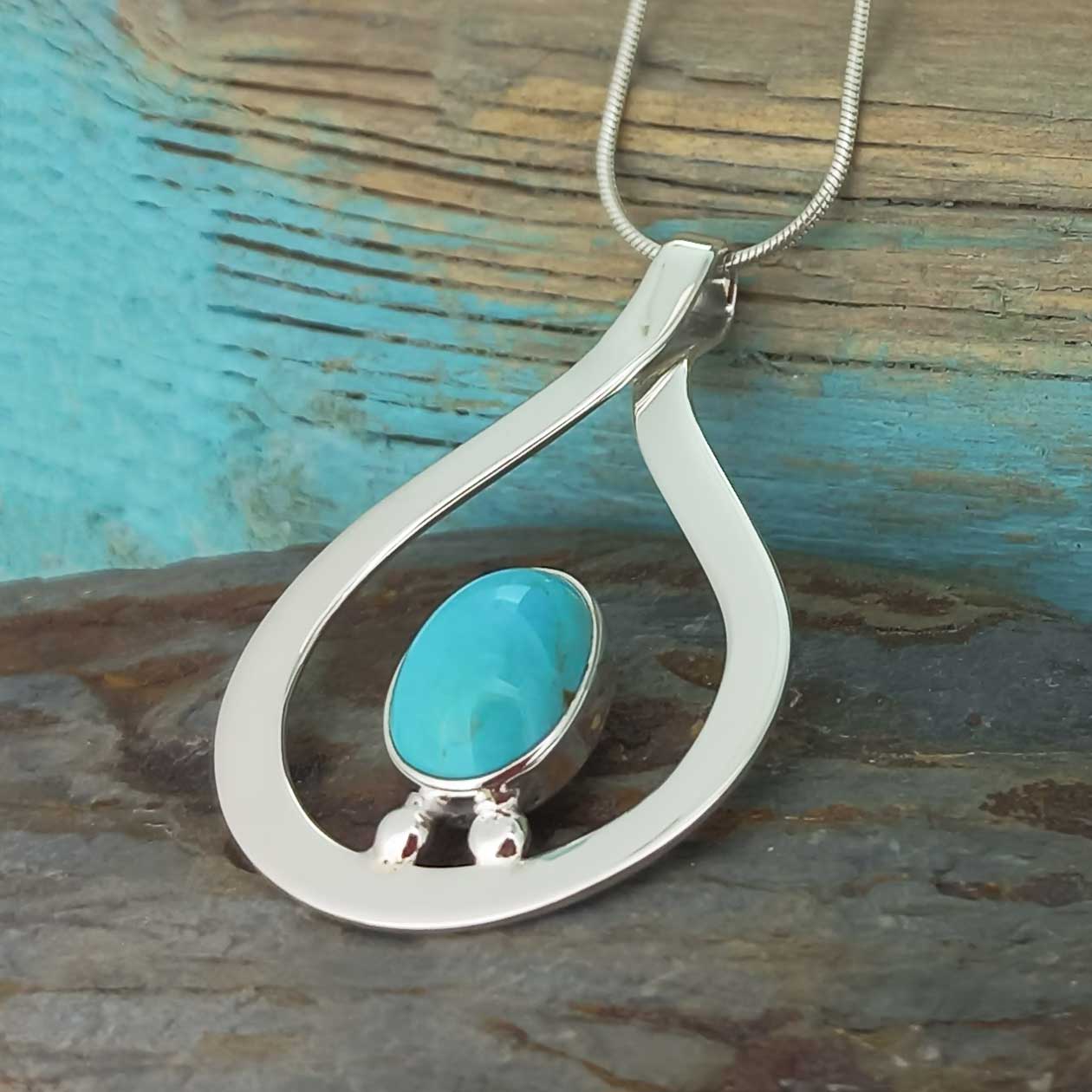 An unusual silver teardrop pendant necklace featuring a smooth, oval-shaped turquoise cabochon stone