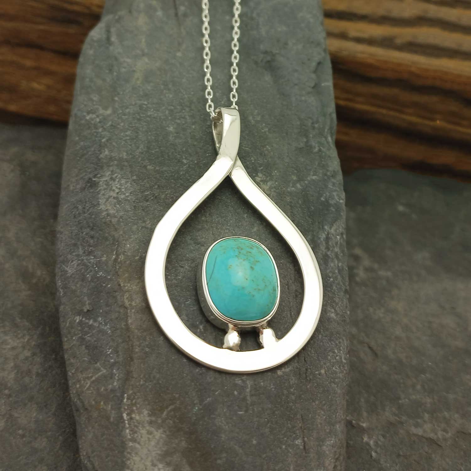 Silver pendant with turquoise stone on a dark stone surface