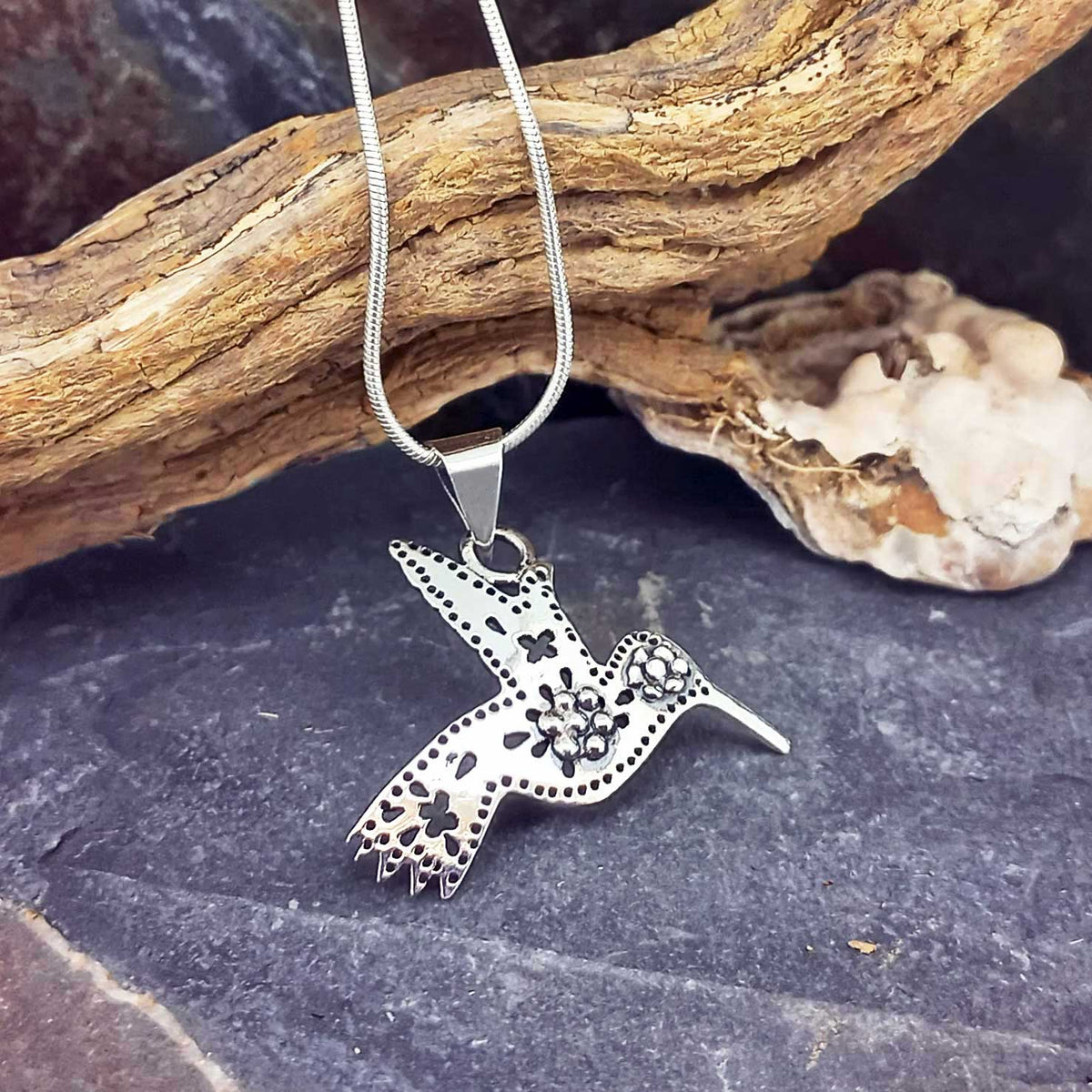 A sterling silver hummingbird pendant necklace with floral and dotted details, hanging from a silver chain.