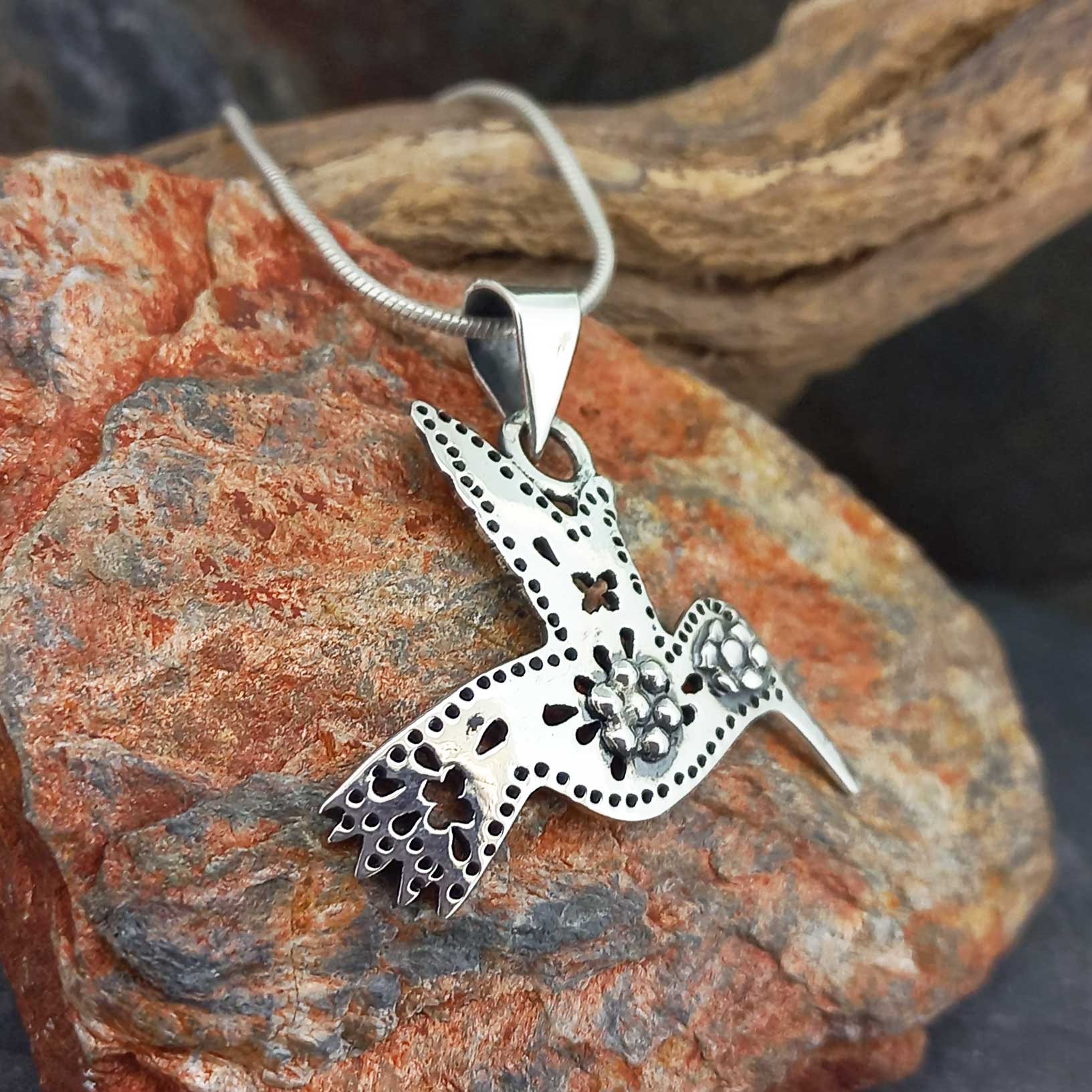 A silver hummingbird pendant necklace with floral filigree details.