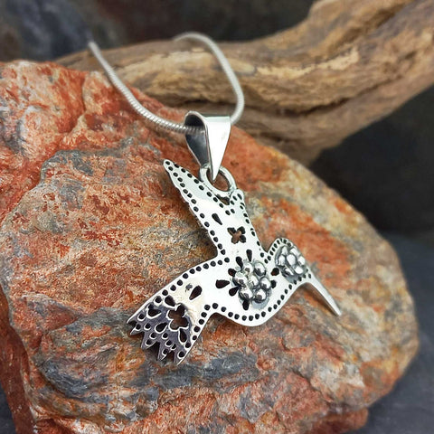 A silver hummingbird pendant necklace with floral filigree details.