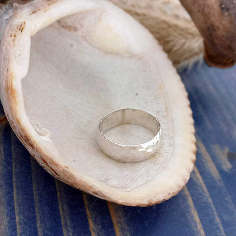 Silver beaten textured ring inside a seashell on a blue striped surface