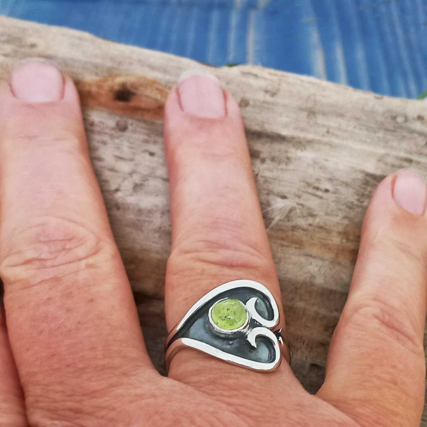 Hand wearing a silver ring with a green Peridot stone on a wooden surface