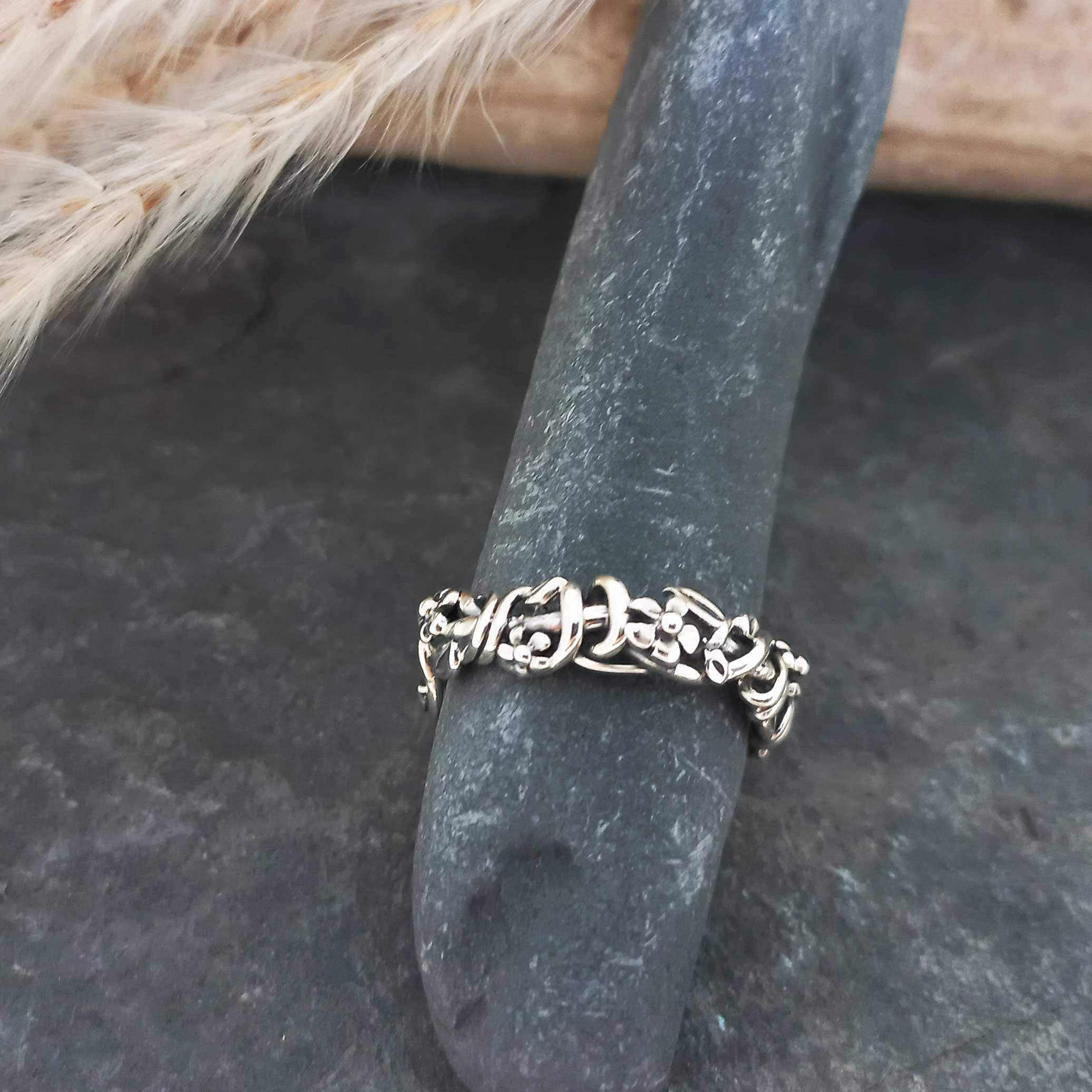 Silver ring with intricate floral design on a dark stone surface