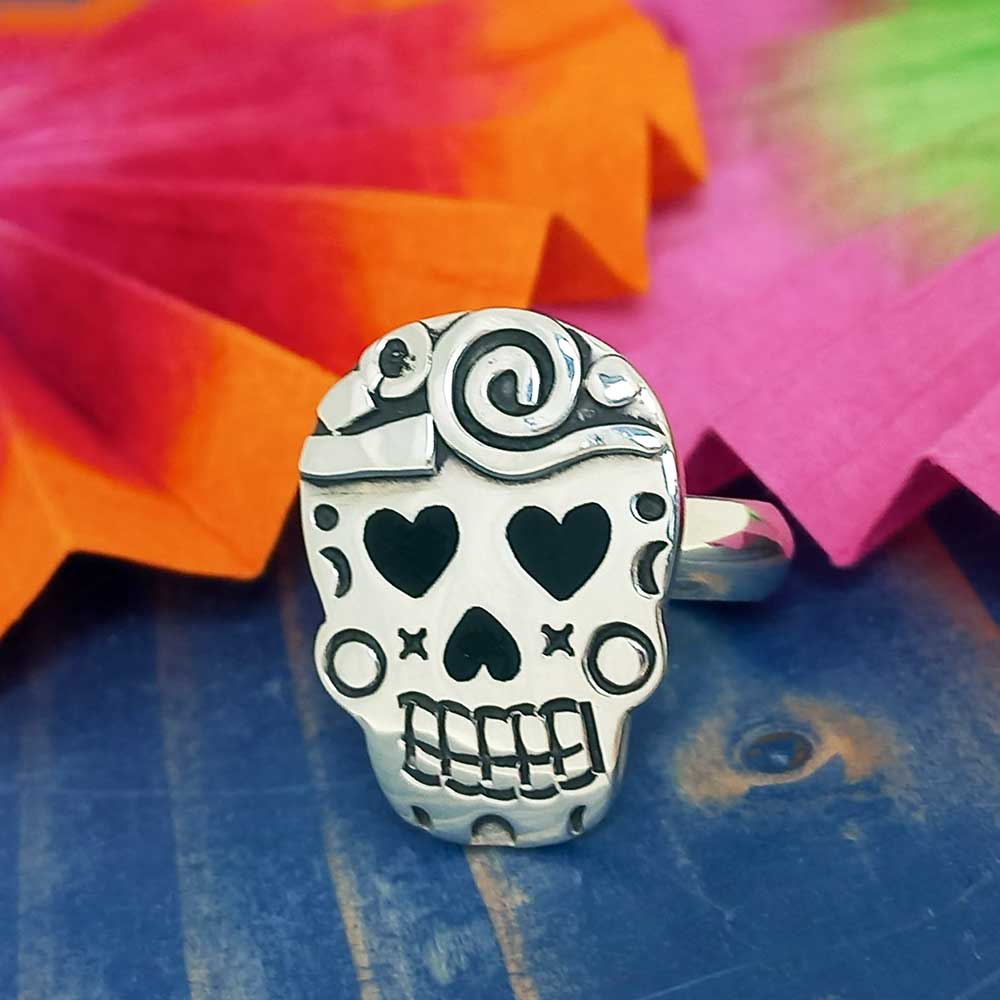 Silver skull-shaped Mexican ring with oxidised details on a colorful fan background