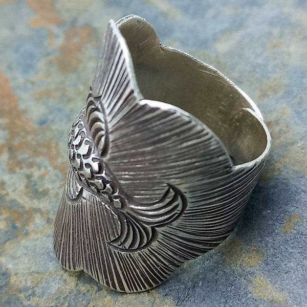 Silver ring with intricate fish design on a textured surface