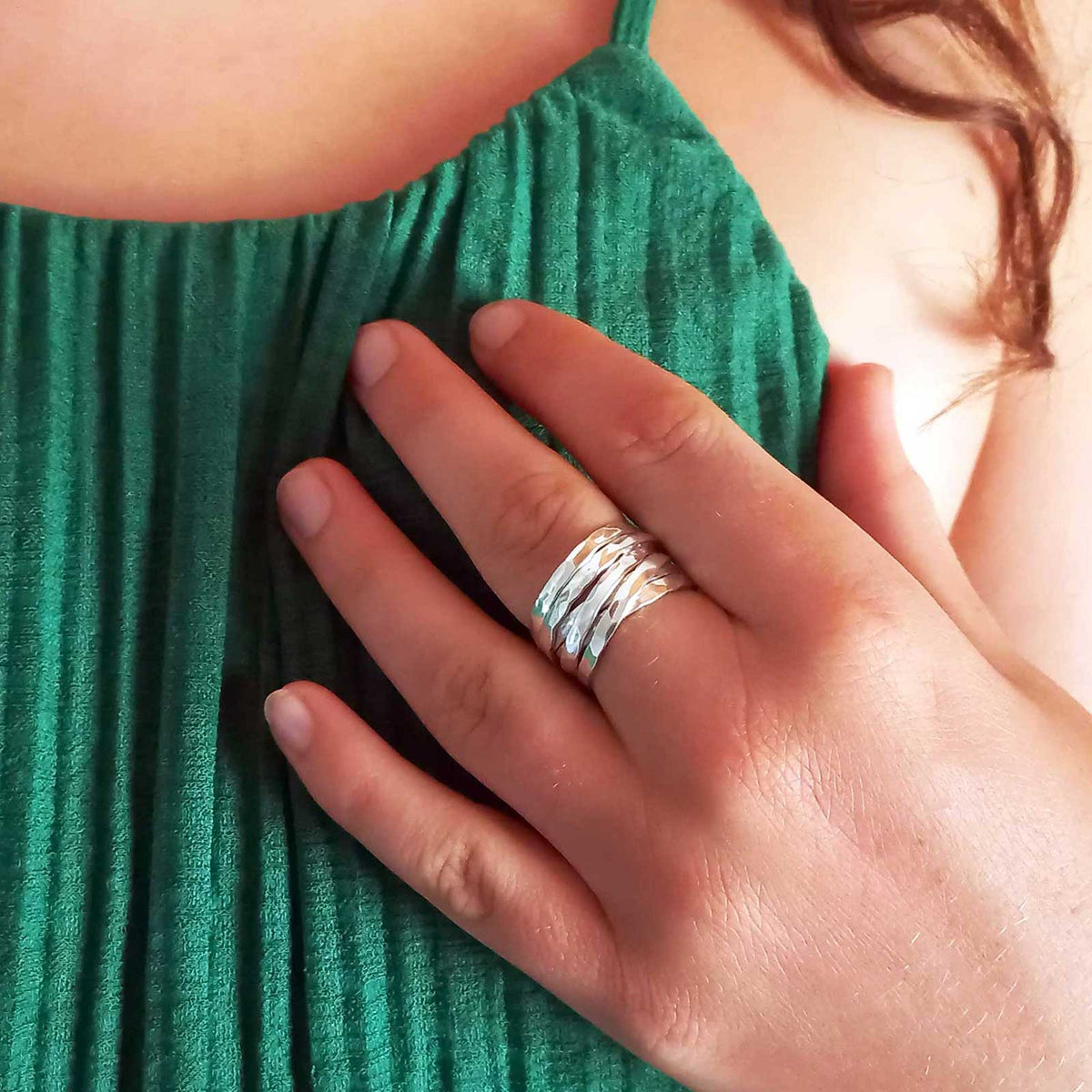 A close-up of a hand wearing a chunky, handmade silver ring with multiple textured bands, resting on a green pleated top.