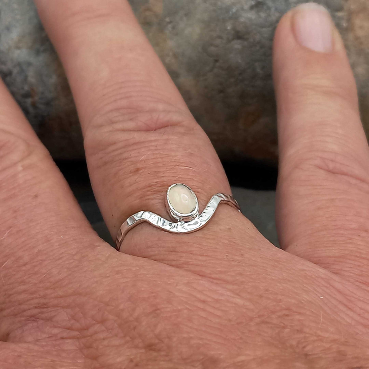 Silver ring with an opal on a person's finger against a stone background