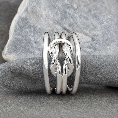 A polished sterling silver ring with a central knotted design and three parallel bands, displayed on a smooth gray stone.