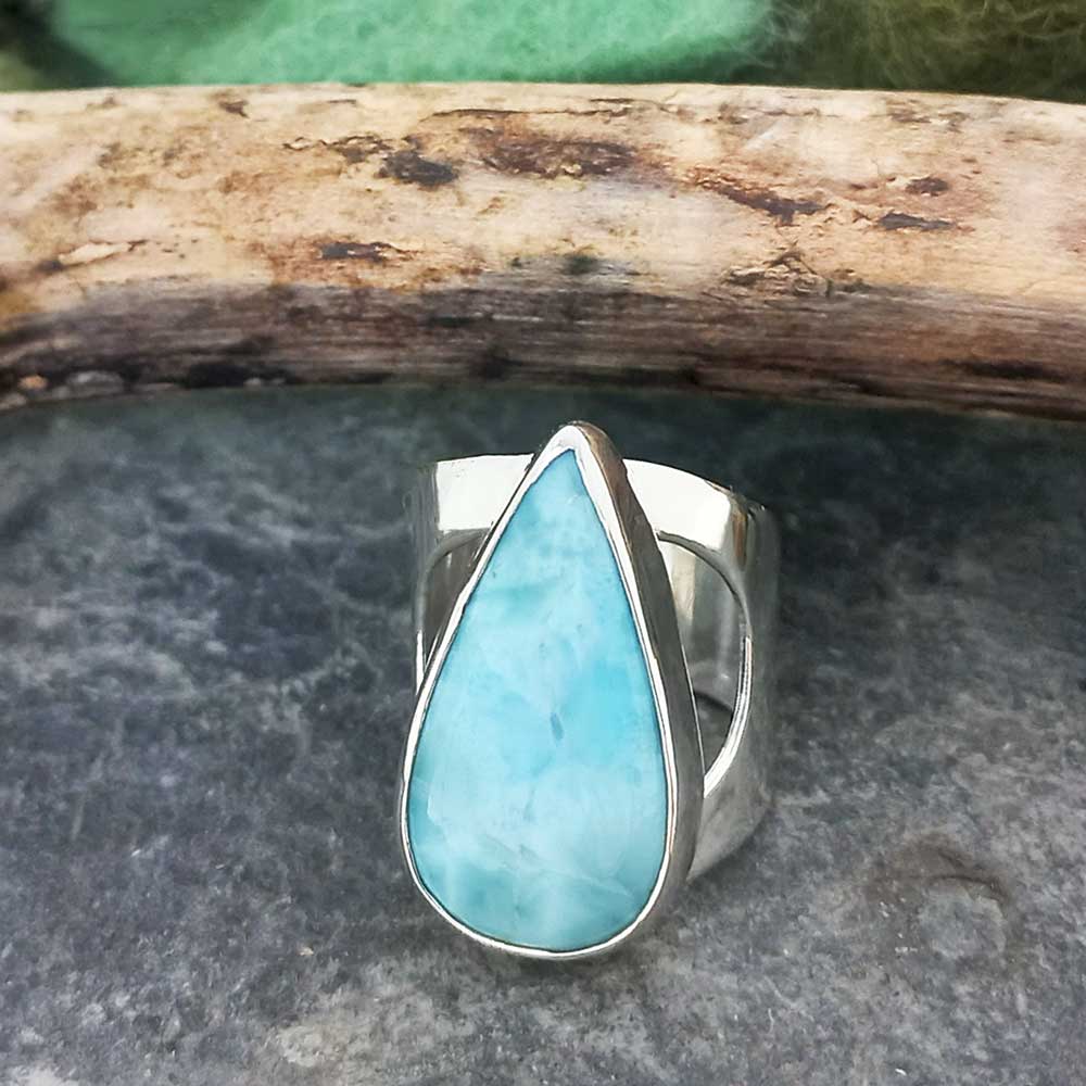 Teardrop-shaped Larimar stone ring on a stone surface with a wooden log in the background