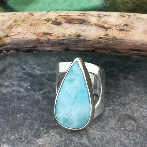 Teardrop-shaped Larimar stone ring on a stone surface with a wooden log in the background