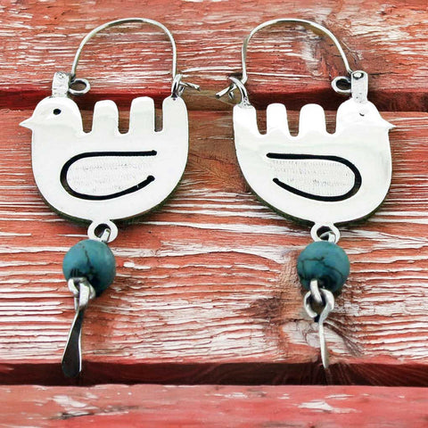 Silver bird-shaped earrings with turquoise beads on a wooden surface