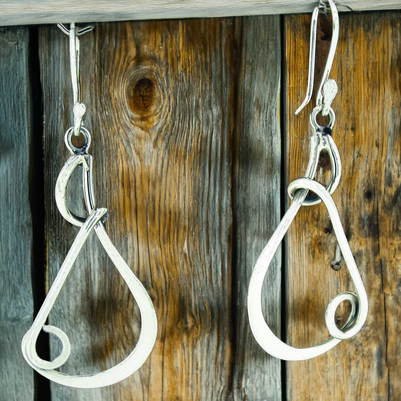 Silver teardrop earrings hanging on a wooden surface