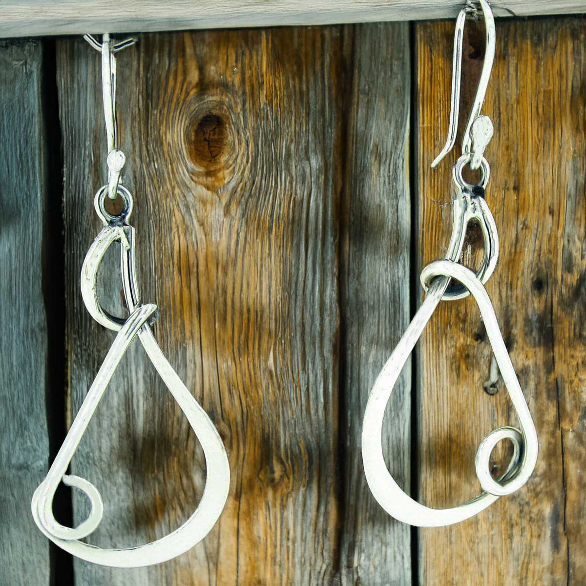 Silver teardrop earrings hanging on a wooden surface
