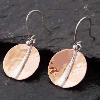 Pair of earrings with round copper discs and silver accents on a dark background