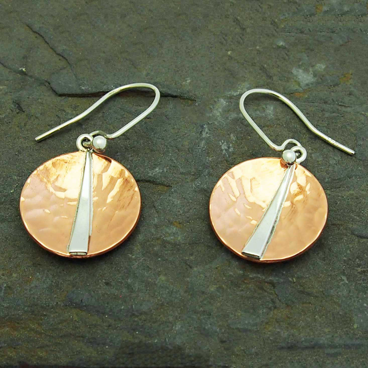 Pair of copper and silver earrings on a dark stone surface