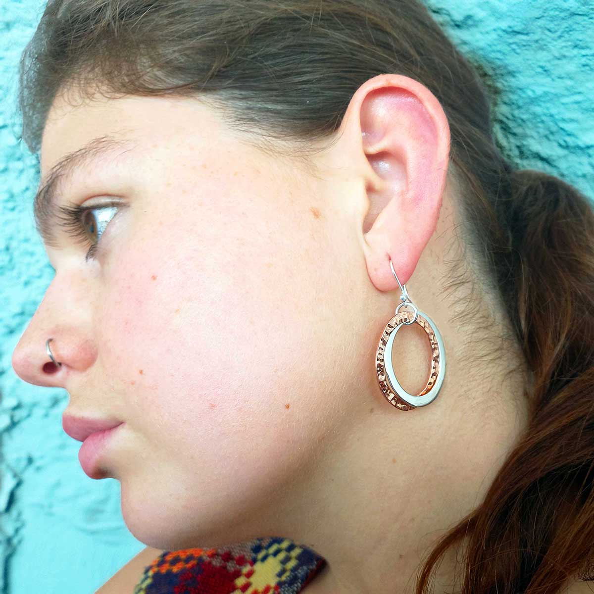Close-up of a person wearing a copper silver hoop earring against a blue background