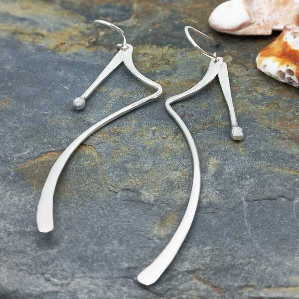 Silver wishbone-shaped earrings on a stone surface