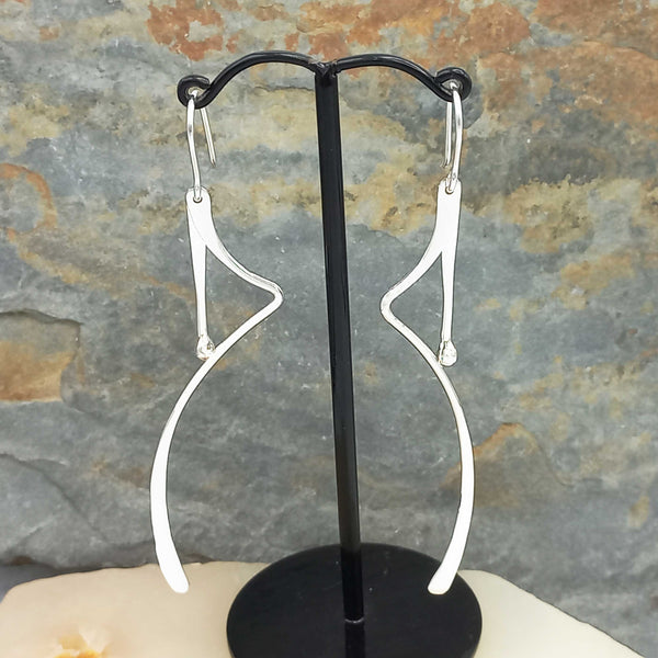 Silver earrings on a black earring stand against a stone wall background