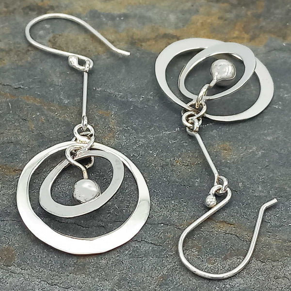 Silver earrings with circular designs on a stone surface