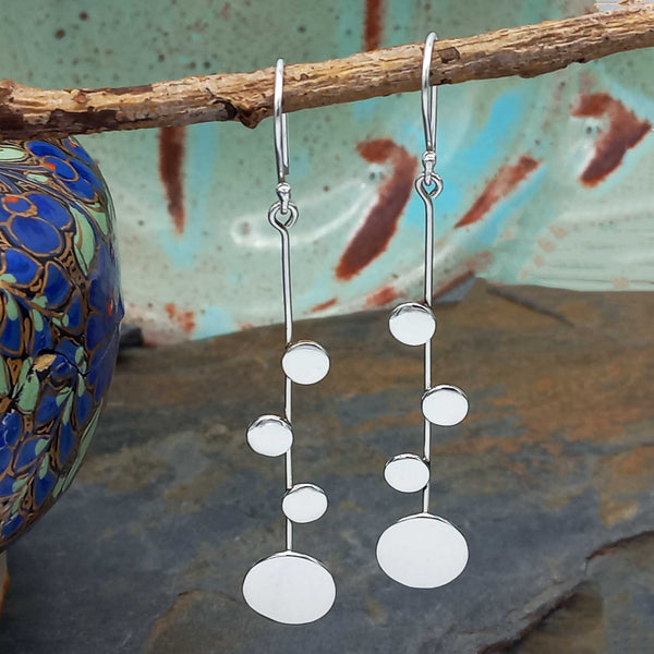 Silver earrings with circular designs hanging from a branch against a textured background