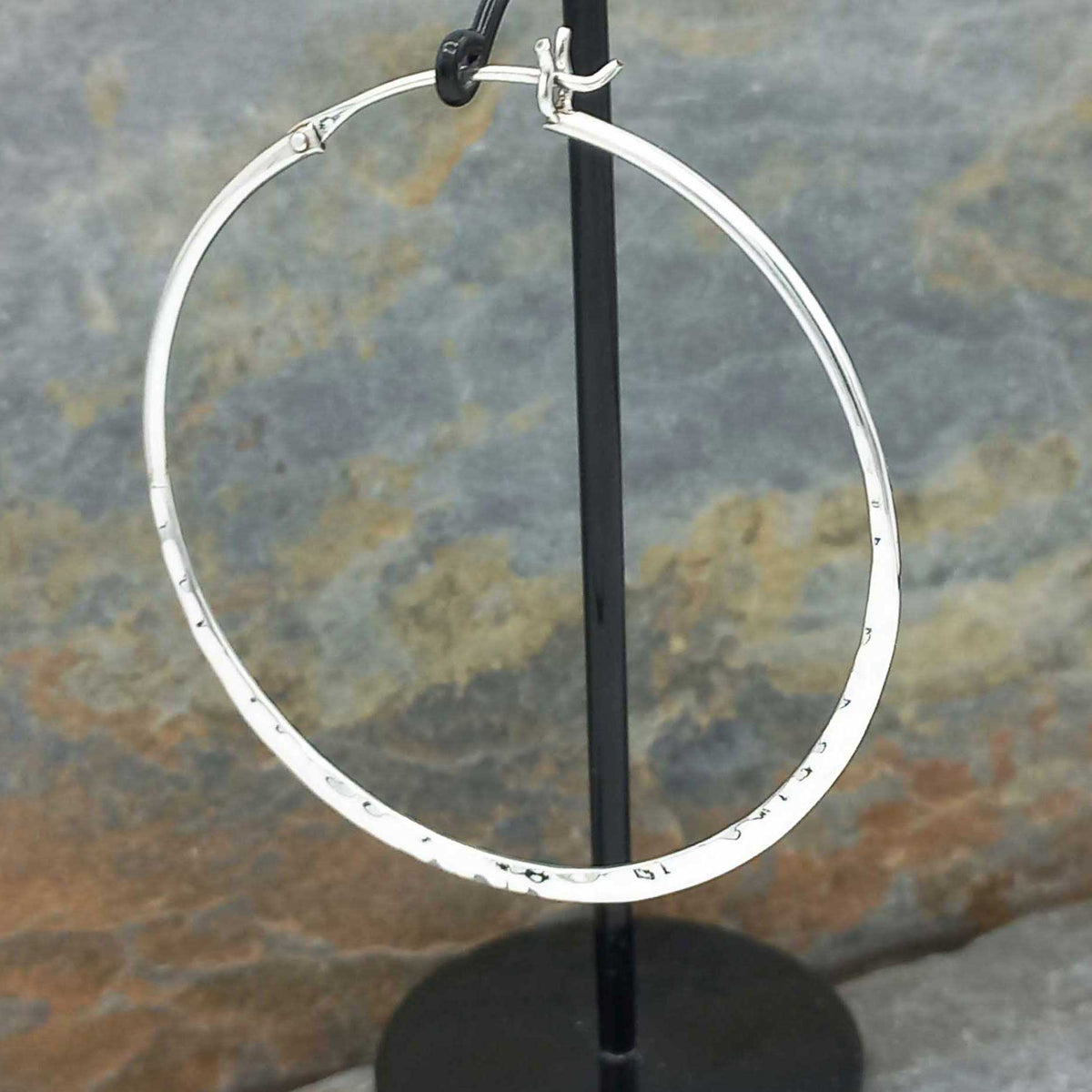 Large silver hoop earring on a stand against a stone background
