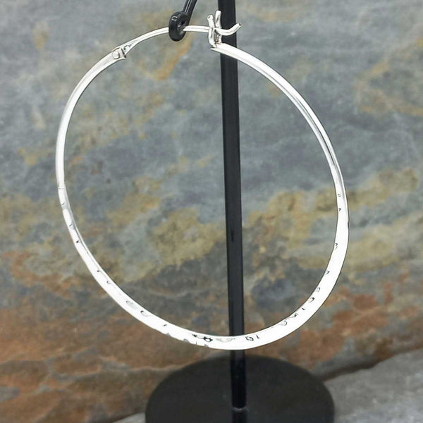 Large silver hoop earring on a stand against a stone background