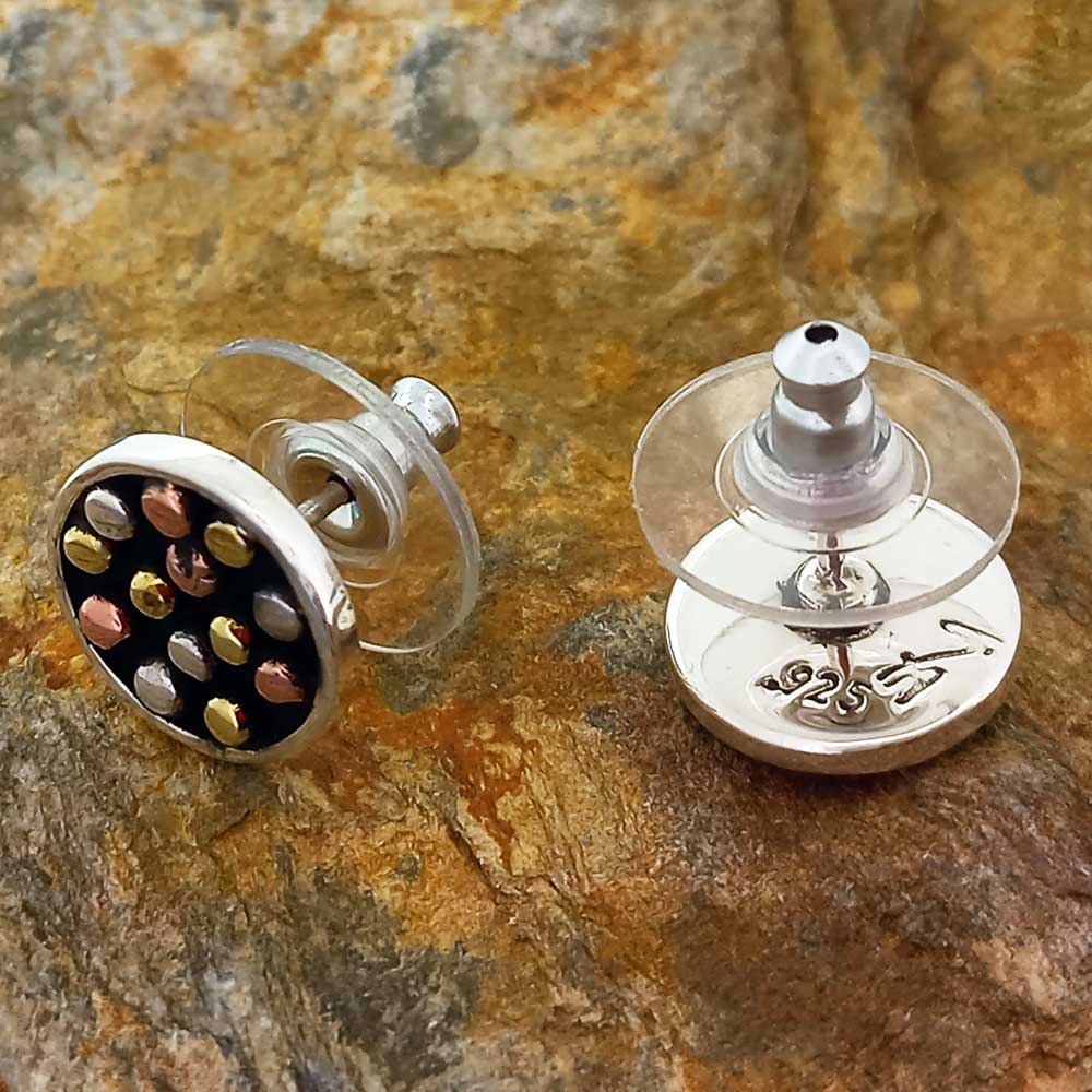 Silver earrings with golden colored dots on a stone surface
