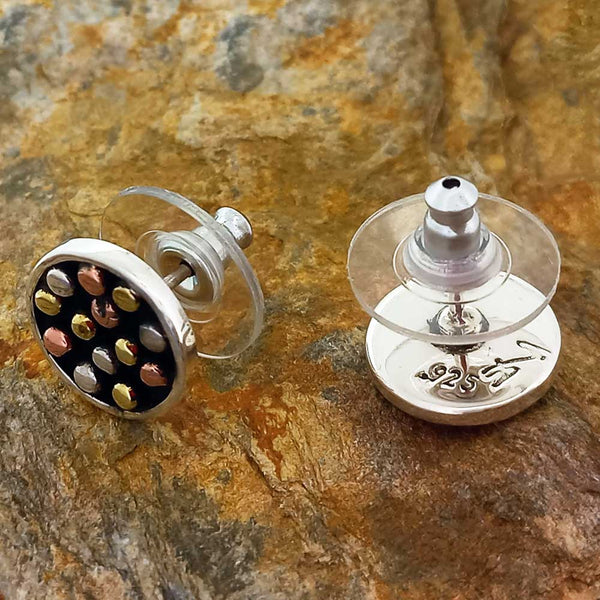 Silver earrings with golden colored dots on a stone surface