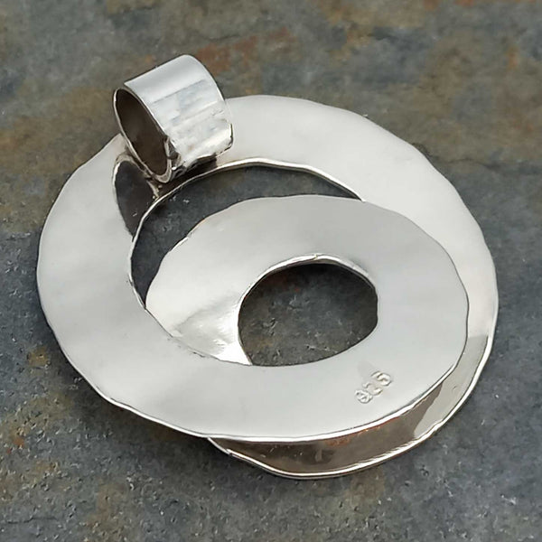 Back of spiral silver pendant on a textured gray surface